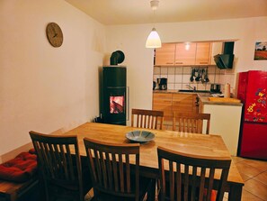 A dining area with a wooden table and chairs, a kitchen with wooden cabinets, a red refrigerator, and a wall clock. - Schnitterhaus Milena on Lake Flee - Milena Vacation Home on Lake Flee (Göhren-Lebbin)