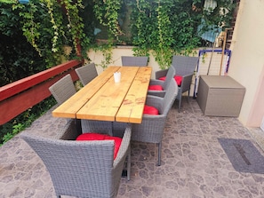 An outdoor patio with a wooden table and wicker chairs, surrounded by greenery. - Schnitterhaus Milena on Lake Flee - Milena Vacation Home on Lake Flee (Göhren-Lebbin)