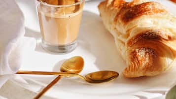 A breakfast setting with a croissant, a glass of coffee, and a spoon on a white table.