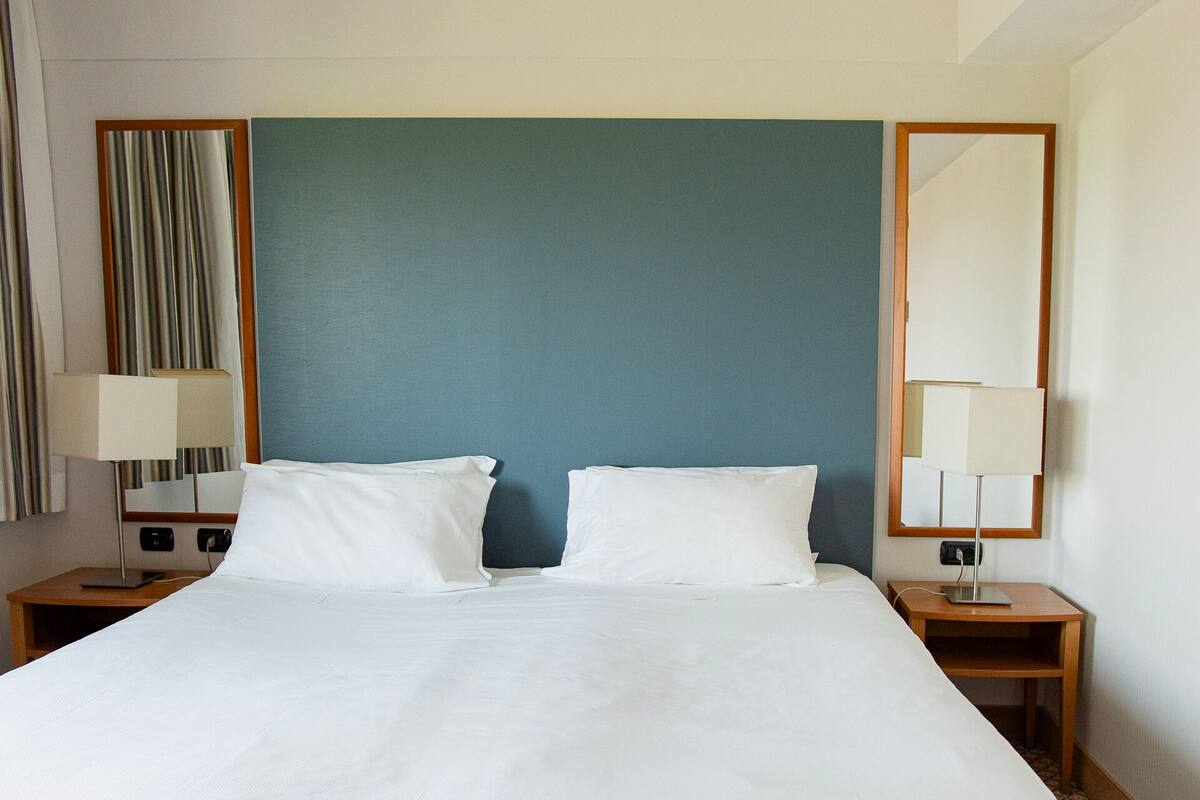 A hotel room with a large bed, two bedside tables, and two wall-mounted lamps.
