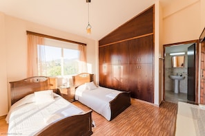 A bedroom with two beds, a wardrobe, a window with curtains, and a bathroom with a sink and mirror. - Villa Leantros -  Privately Set Villa near the Sea sleeping 8 guests in 4 bedrooms (Paphos)