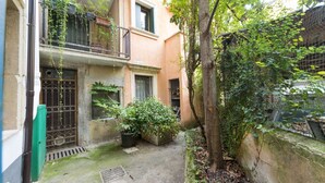 A narrow courtyard with a tree, potted plants, and a metal gate.