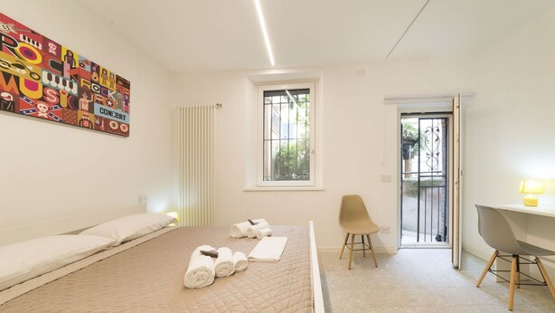 A hotel room with a bed, a desk, a chair, a window, and a radiator.