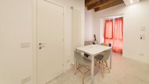 A room with a white door, a radiator, a table with chairs, and a window with red curtains.