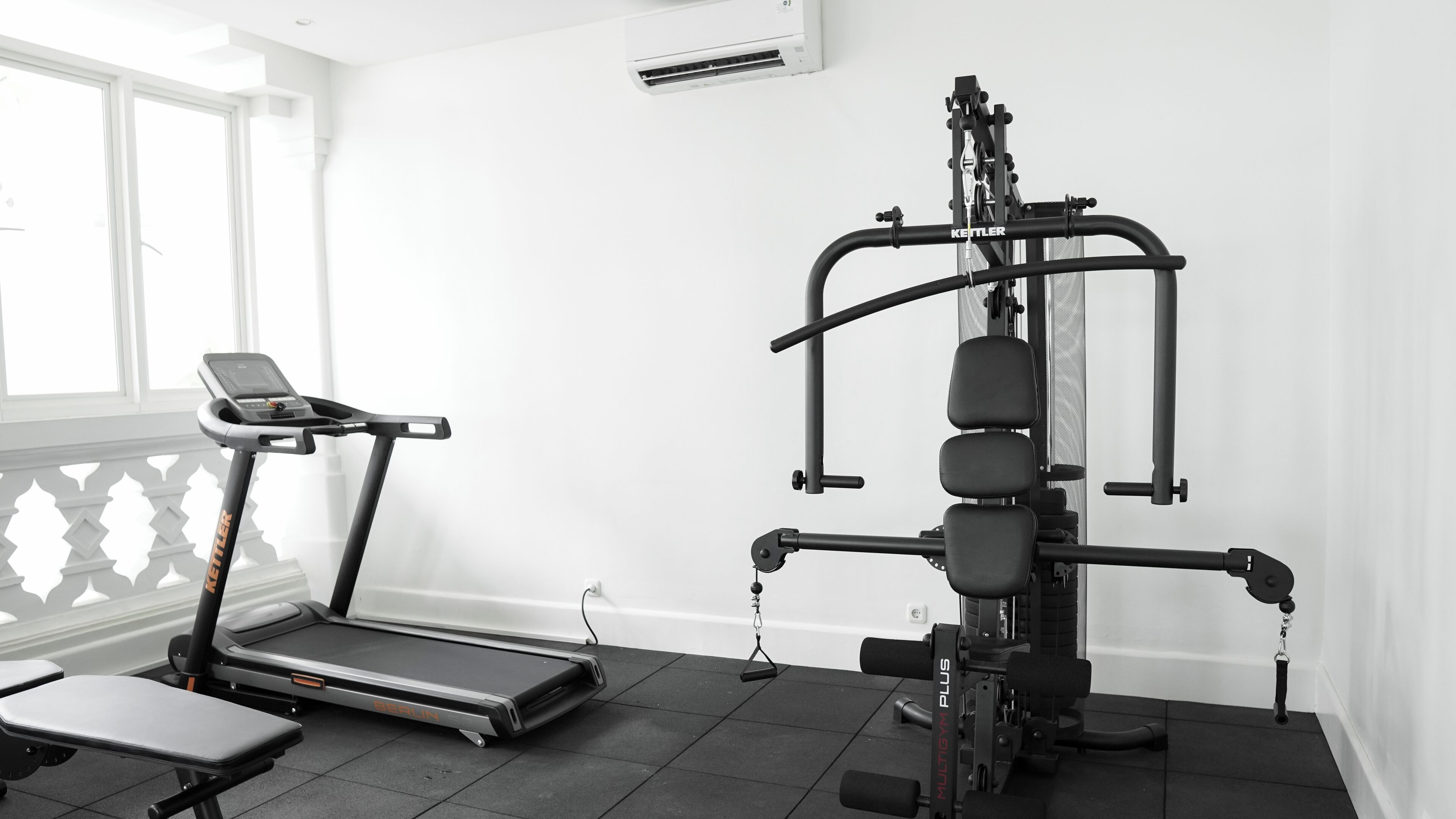 Een sportschool met een loopband, een gewichtbank en een multifunctionele fitnessapparaat.