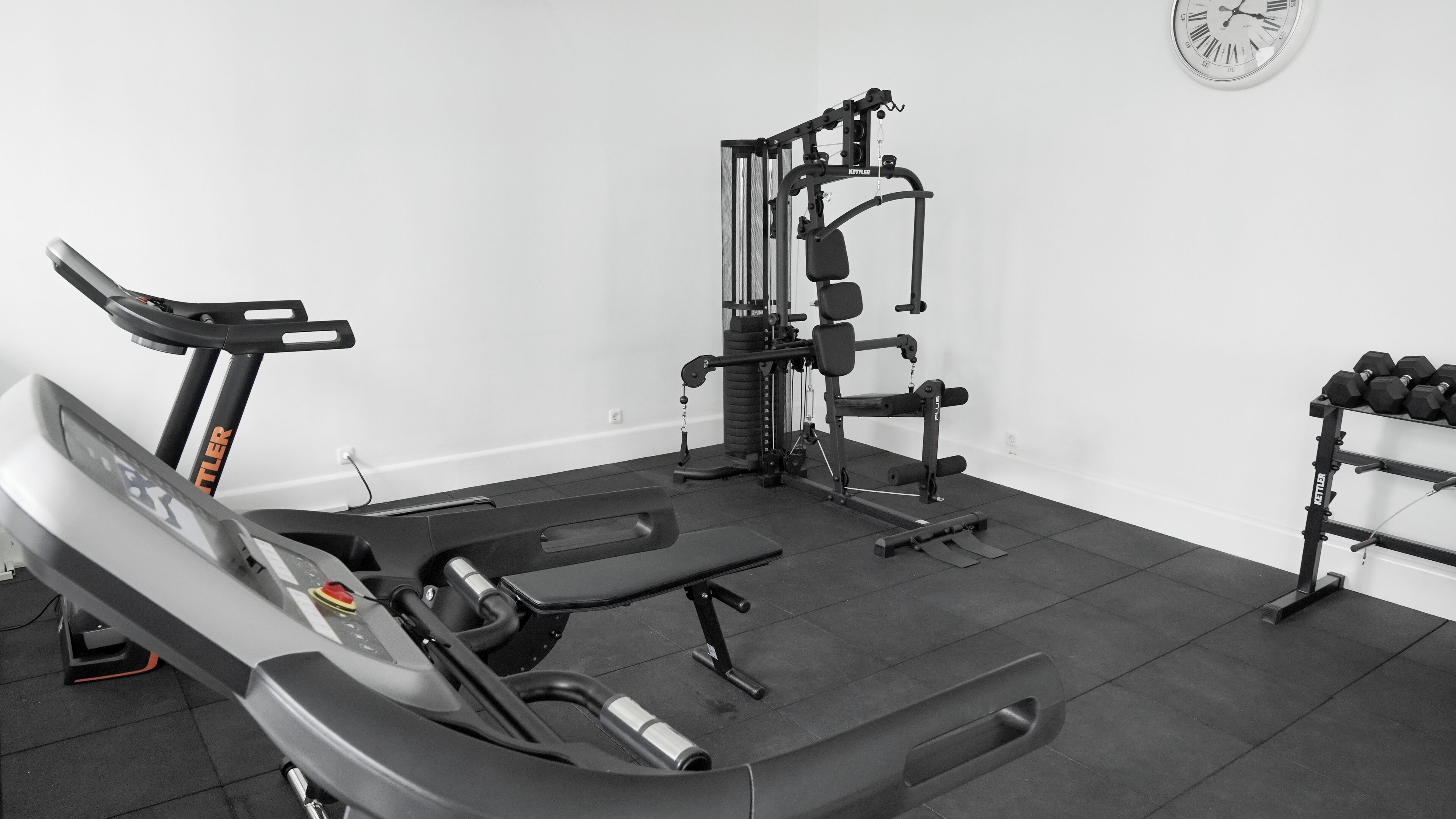 Uma academia com esteira, banco de musculação e diversos equipamentos de ginástica.