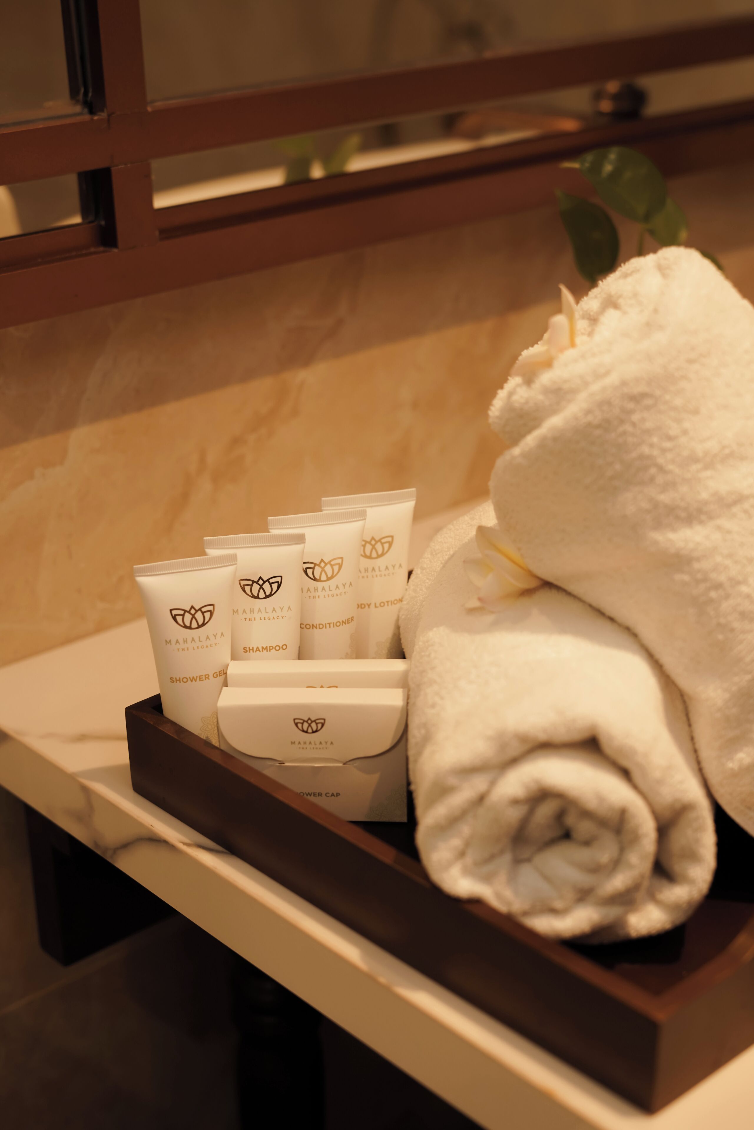 Bandeja com shampoo e condicionador Mahalaya The Legacy, uma toalha dobrada e um touca de banho.