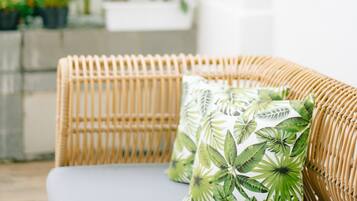 A wicker sofa with a white cushion and a green leaf-patterned pillow.