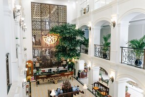 A grand lobby with a large decorative screen, a central plant, and a seating area with a piano.