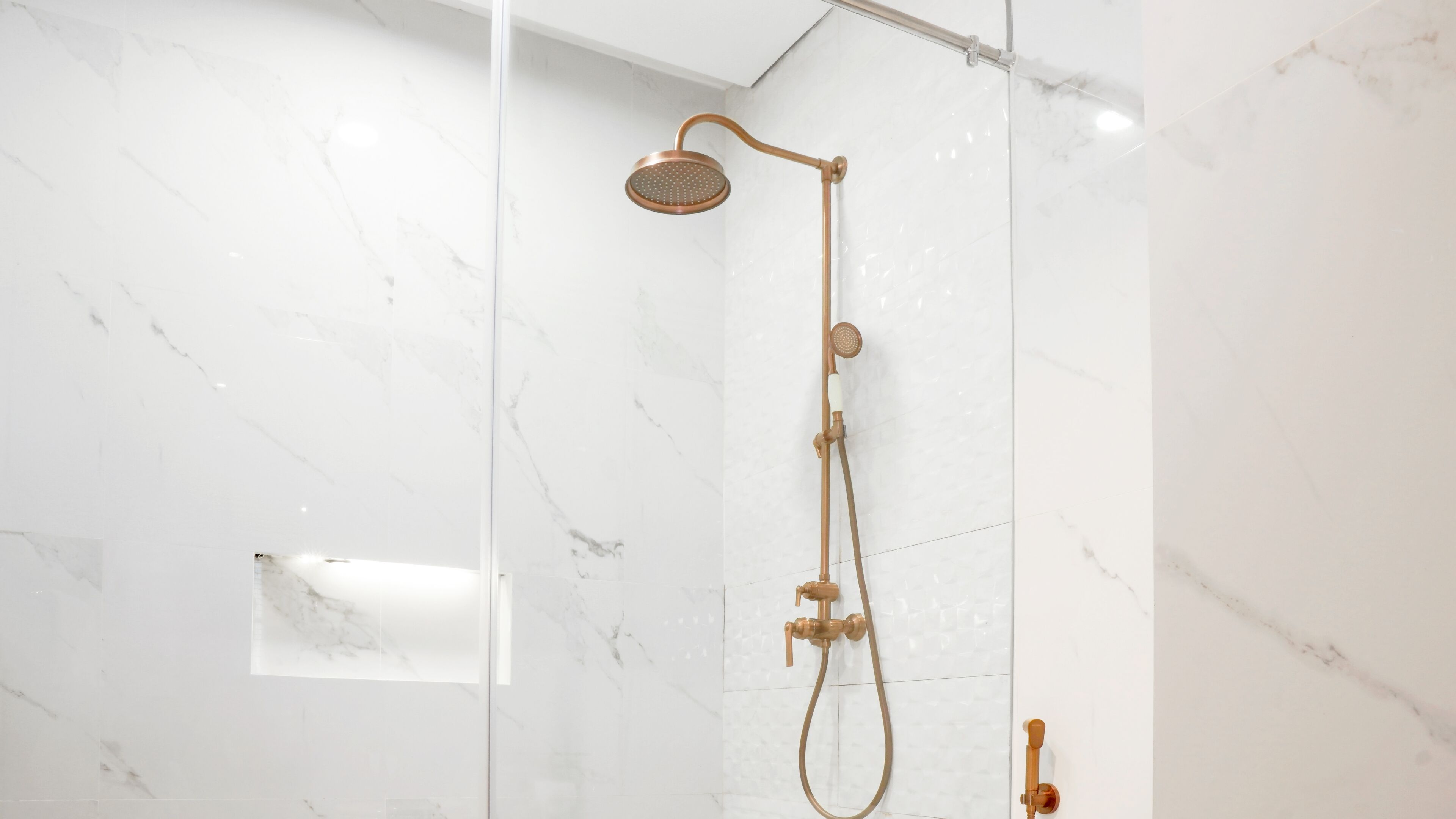 A modern bathroom with a glass-enclosed shower, marble walls, and a gold-colored showerhead.
