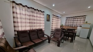 A living room with a sofa, chairs, a dining table, and a kitchen area with a refrigerator.