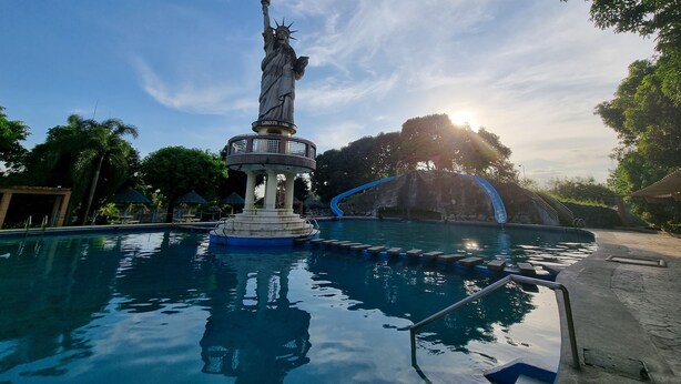 A statue in a pool area with a clear sky and trees in the background.
