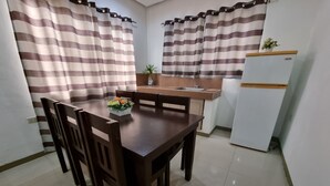A compact kitchen with a dining table, chairs, a refrigerator, and striped curtains.
