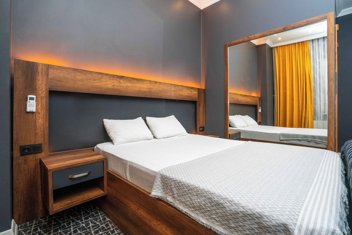 Une chambre d’hôtel moderne avec un grand lit, une tête de lit en bois, des tables de chevet et un miroir.