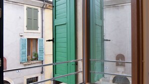 A narrow street with buildings featuring green shutters and a visible balcony railing.