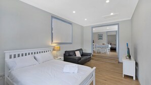 Een slaapkamer met een bed, een nachtkastje, een zwarte leren bank, een zithoek met een tafel en stoelen, en een televisie op een dressoir.