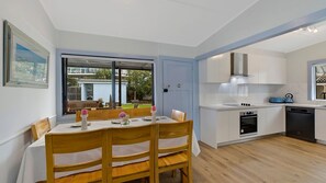 Une cuisine moderne avec des armoires blanches, un four encastré et un coin repas comprenant des chaises et une table en bois.