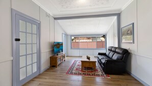 Een ruime woonkamer met een houten vloer, een zwarte leren bank, een salontafel en een tv op een houten dressoir.