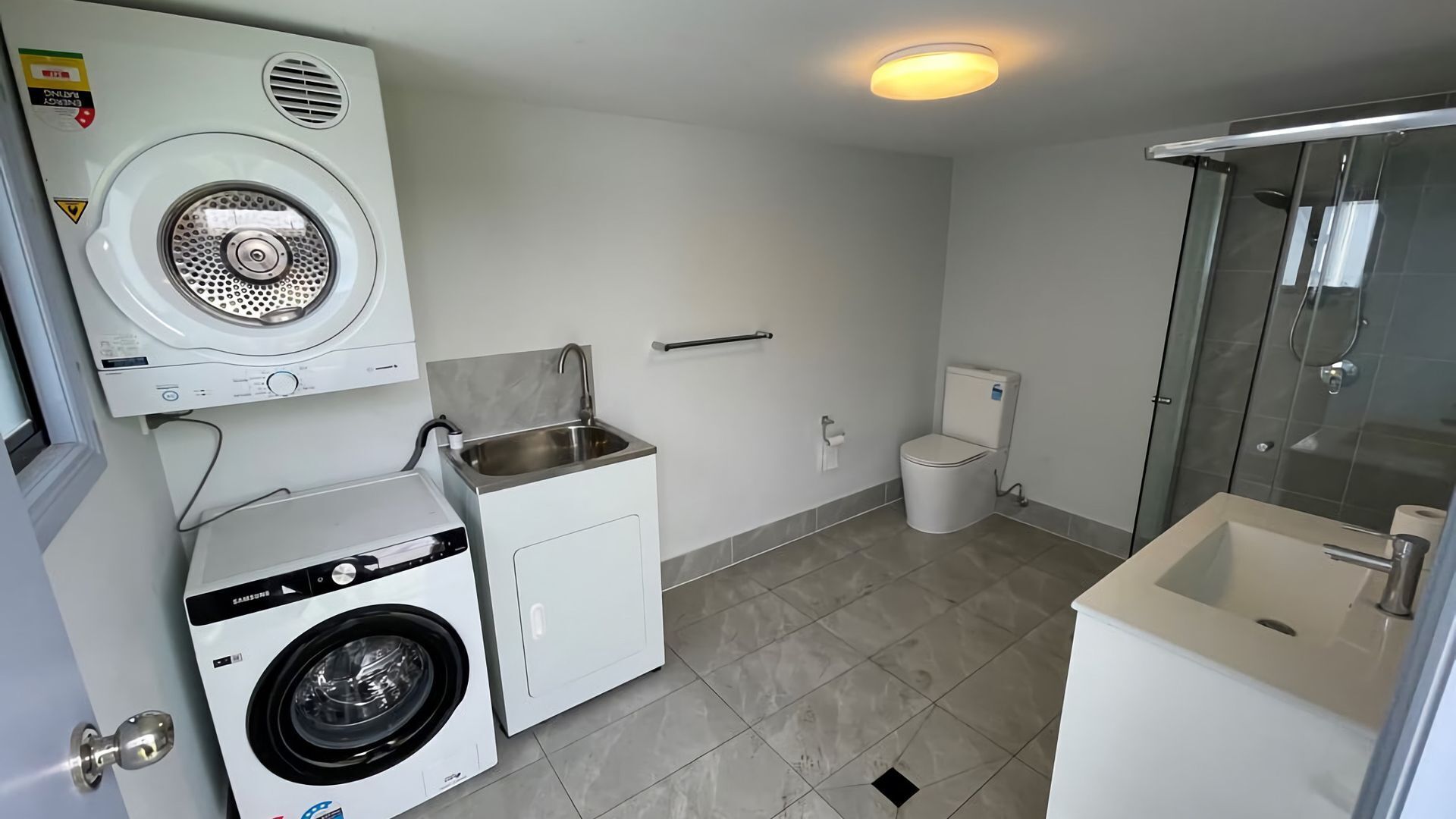 Een compacte, moderne badkamer met een wasmachine, toilet en douche.