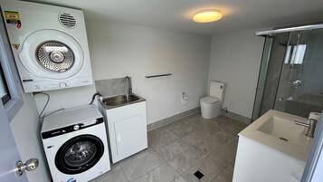 Een compacte, moderne badkamer met een wasmachine, toilet en douche.