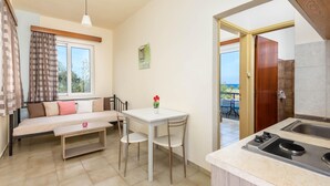 A compact living space with a sofa, dining table, chairs, a small kitchen area with a sink, and a view of the outdoors. - Litsas Studios (Rhodes)