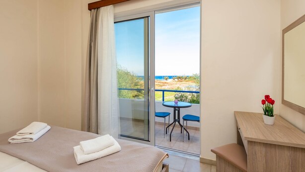 A hotel room with a bed, a desk, a chair, and a balcony with a view. - Litsas Studios (Rhodes)
