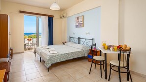 A hotel room with a bed, a dining table with chairs, a balcony with a view of the sea, and a painting on the wall. - Litsas Studios (Rhodes)