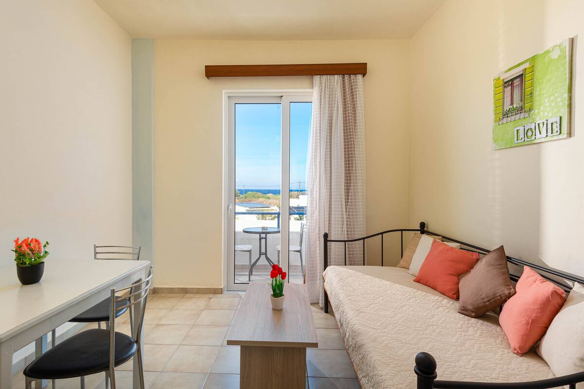 Un dormitorio con cama, una mesa con sillas, una ventana con cortinas y vistas al exterior.