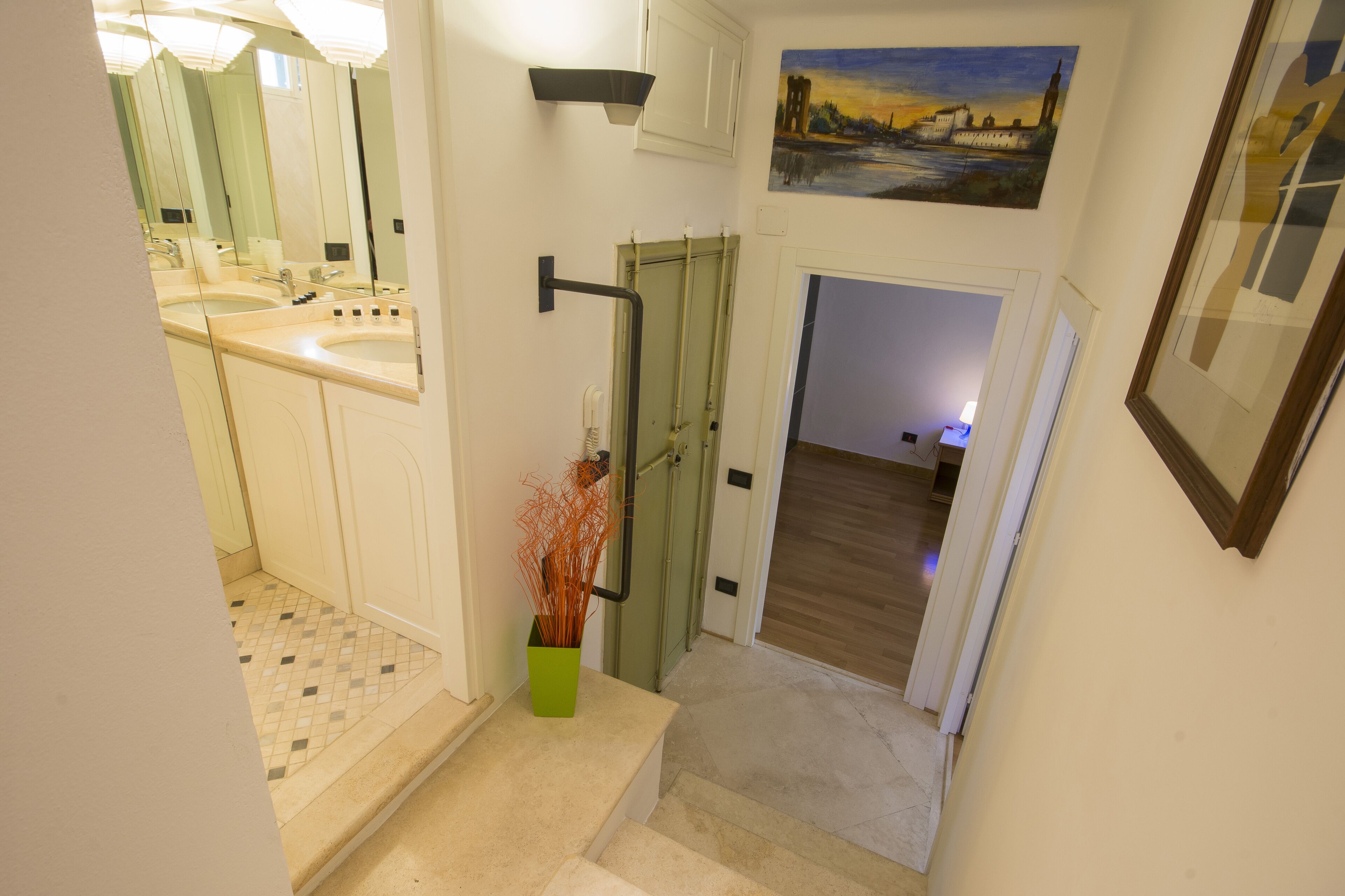 A hallway with a bathroom, a green door, and a painting on the wall.