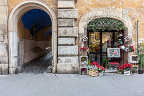 A storefront with a stone facade, an archway entrance, and various potted plants and flowers displayed outside. - Rome Historical Apartment - Arco dei Banchi (Roma)