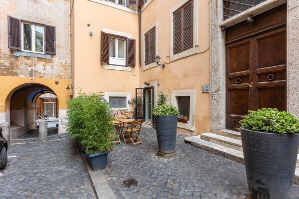 A cobblestone street with a wooden table and chairs, potted plants, and a large wooden door.