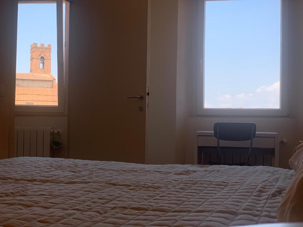 Ein Schlafzimmer mit Bett, Sessel und Fenster mit Blick auf einen Turm.
