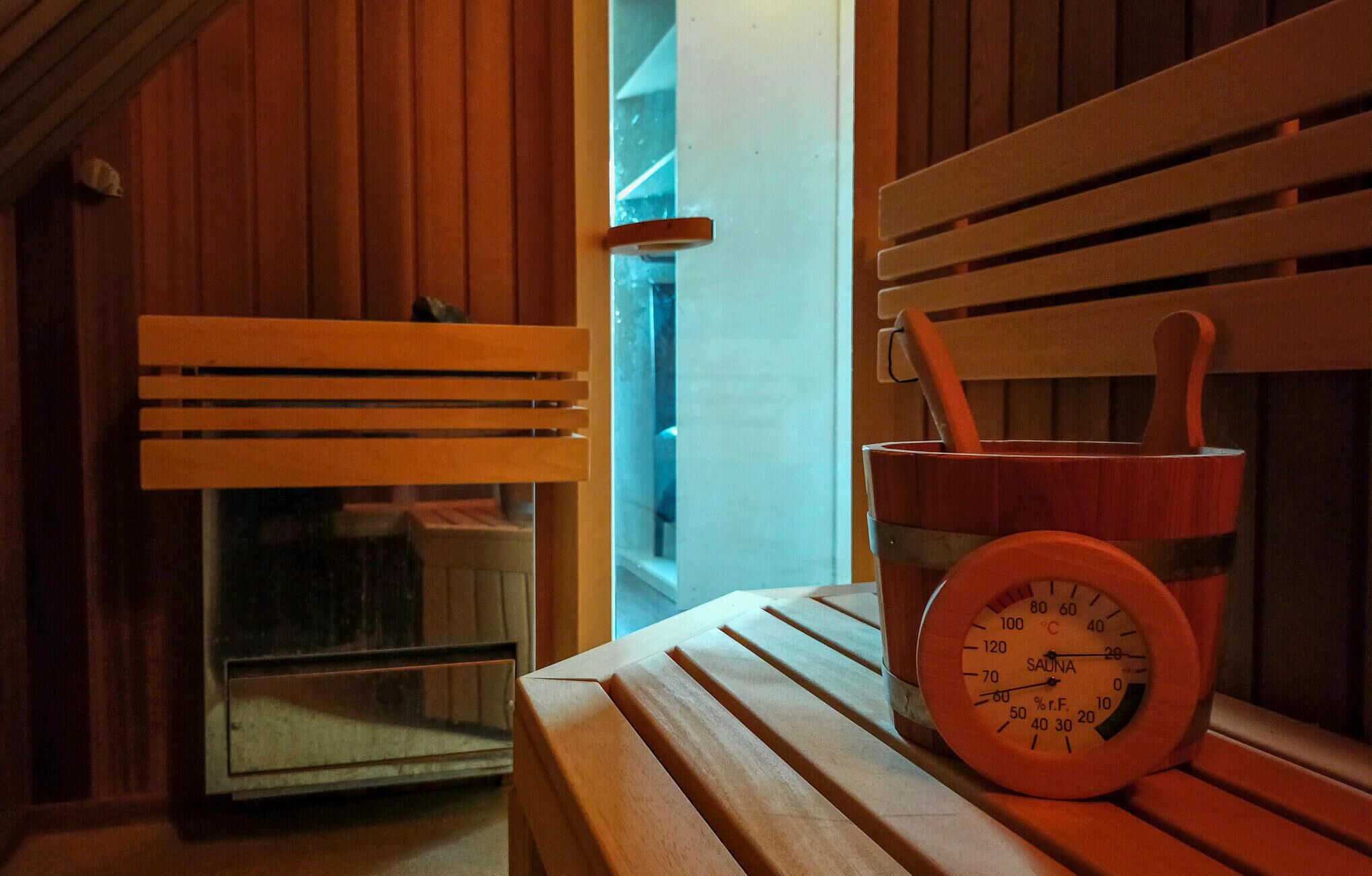 A sauna with wooden benches and a wooden bucket with a thermometer.