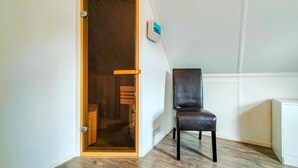 A room with a wooden door, a black leather chair, and a white wall with a blue device.