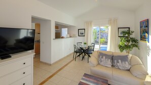 A modern living room with a flat-screen TV, a sofa, a dining table with chairs, and a kitchen area in the background. - C2, en pequeño complejo con piscina comunitaria a 100m del mar (Charco del Palo)
