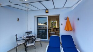 A covered patio with a table and chairs, a lounge area with blue chairs, and an orange umbrella. - C2, en pequeño complejo con piscina comunitaria a 100m del mar (Charco del Palo)