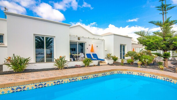 A modern house with a swimming pool, a patio with lounge chairs, and tropical plants. - C2, en pequeño complejo con piscina comunitaria a 100m del mar (Charco del Palo)