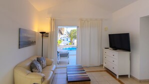 A modern living room with a sofa, a TV, and a view of a pool and outdoor area. - C2, en pequeño complejo con piscina comunitaria a 100m del mar (Charco del Palo)