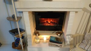 Ein gemütliches Wohnzimmer mit Kamin, einem kleinen Tisch mit Laterne und einem Sessel.