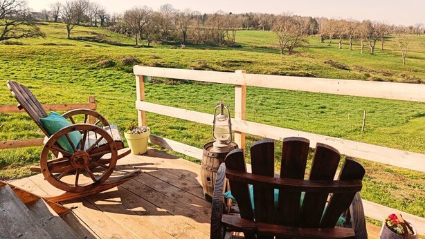 Eine Holzterrasse mit einem Schaukelstuhl und einem Adirondack-Stuhl mit Blick auf ein grünes Feld.