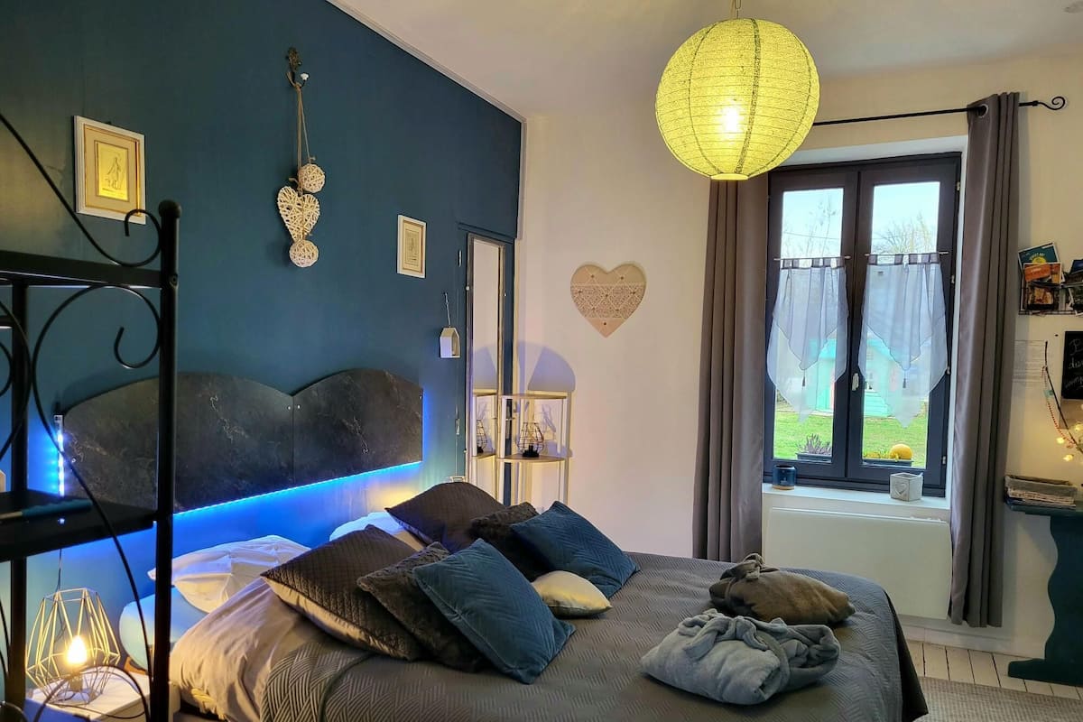 Un dormitorio con cama, mesita de noche y ventana con cortinas.