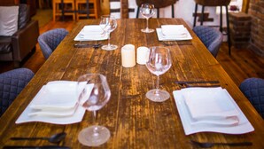 Un tavolo da pranzo in legno apparecchiato con tovaglioli bianchi, bicchieri da vino e posate.