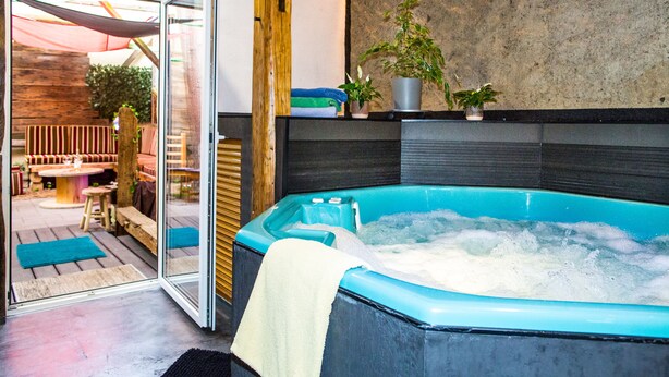 Un'area benessere con vasca idromassaggio, panche in legno e piante in vaso.