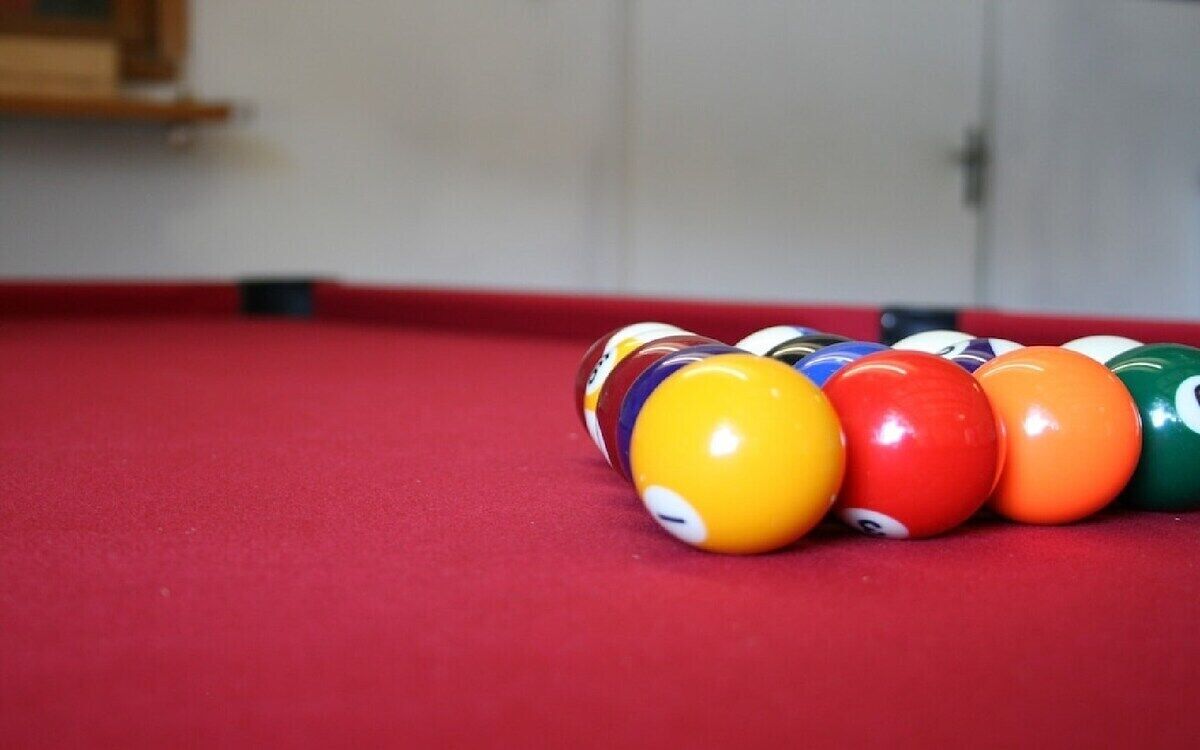 Ein Billardtisch mit roter Spielmatte und einer Reihe bunter Billardkugeln.