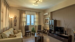 A living room with a sofa, chairs, a coffee table, a TV, and a large window with curtains. - Tranquil Villa overlooking the Cretan sea (Arkadi)