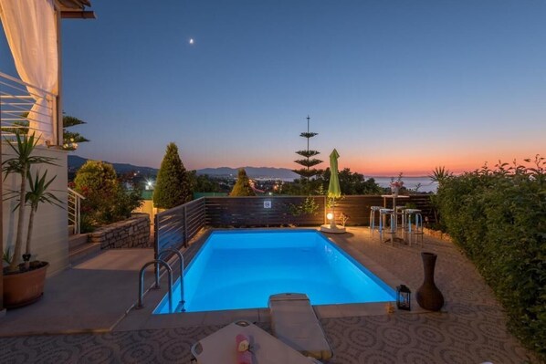 A rooftop swimming pool with a view of the sunset and mountains in the background.