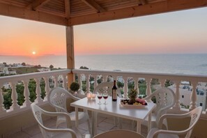 A balcony with a table set for two, overlooking a sunset over the sea.
