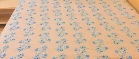 Un lit recouvert d’une couvre-lit à motifs floraux, avec des coussins assortis, dans une pièce aux murs orange.