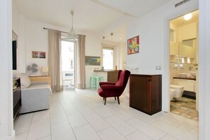 Un soggiorno moderno con un divano, una poltrona rossa, un'area pranzo e una cucina con lavello e servizi igienici visibili.