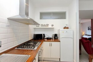 Una cucina compatta con piano cottura a gas, forno a microonde e mobili bianchi.